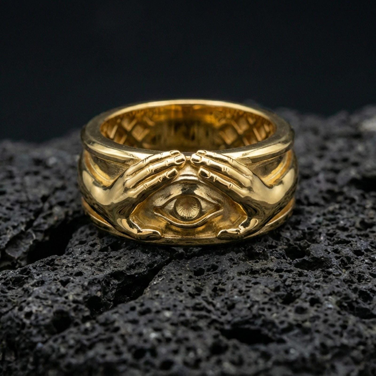 Gold plated protective eye ring on volcanic stone, luxury macro photo capturing warm gold tone across the hands and the central all-seeing eye motif.