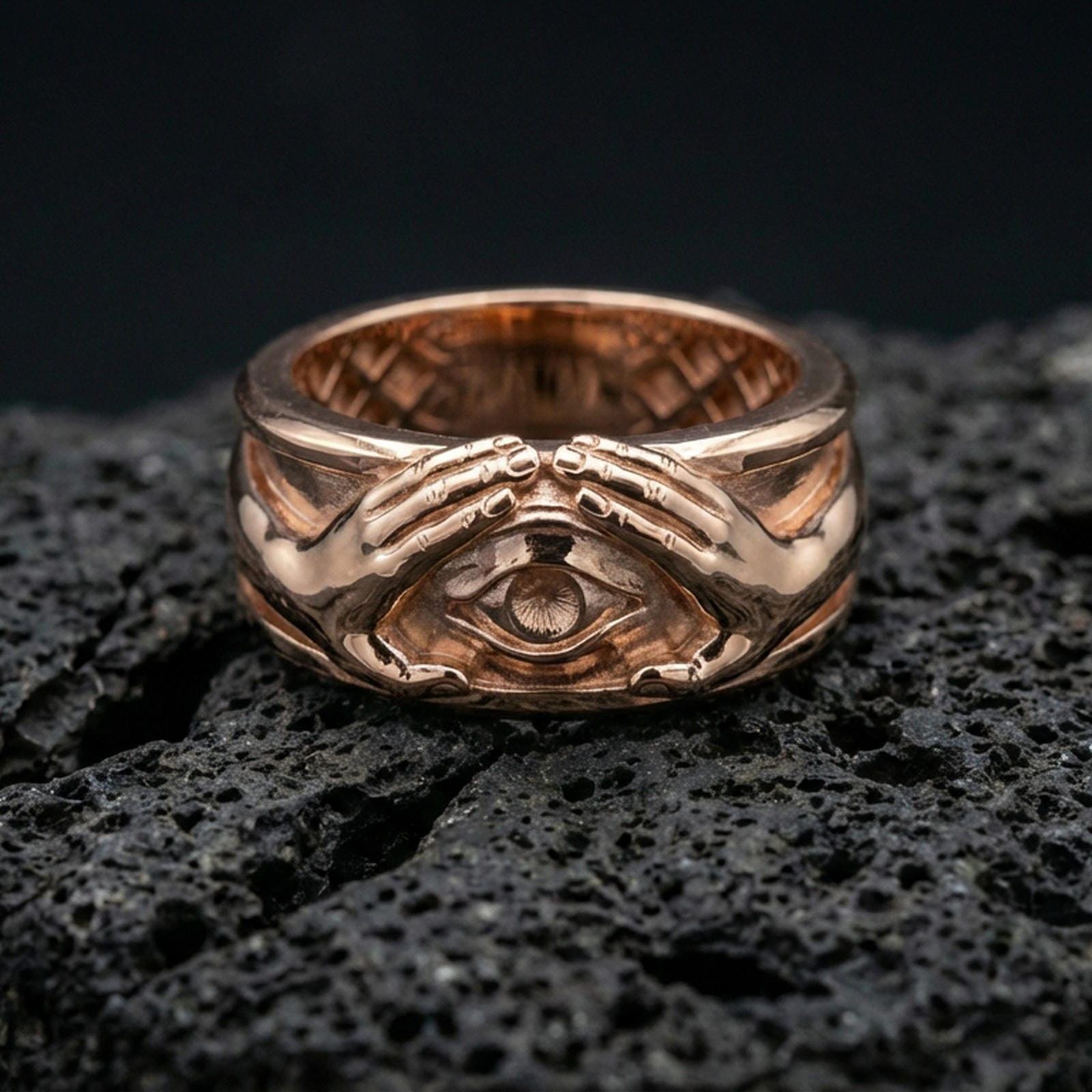 Rose gold plated protective eye ring on volcanic stone, refined macro close-up showcasing soft rose warmth, dimensional hand sculpture, and detailed eye centerpiece.
