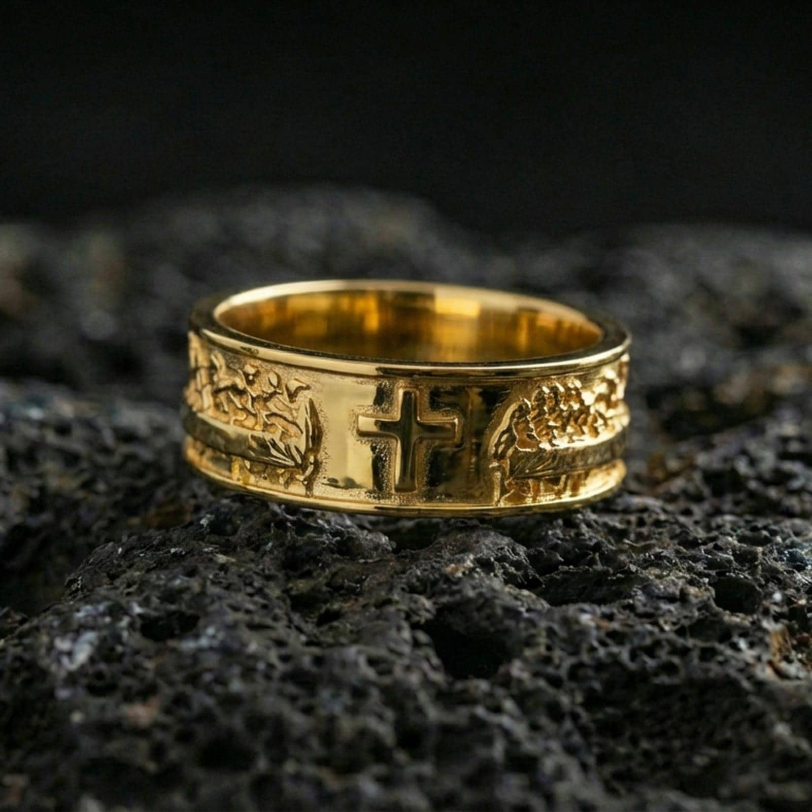 Gold plated cross band ring on volcanic stone, premium macro photo capturing warm gold tone on the raised cross and the surrounding engraved pattern.