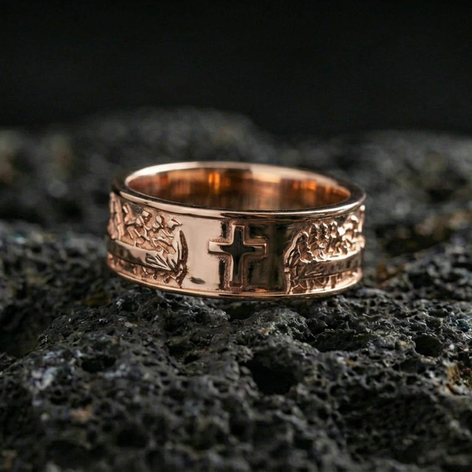 Rose gold plated cross band ring on volcanic stone, refined macro close-up showcasing soft rose warmth, sculpted cross focal point, and high-relief accents.