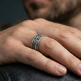Load image into Gallery viewer, Oxidized sterling silver cross band ring worn on the finger, lifestyle image showing bold contrast, elevated cross centerpiece, and a rugged unisex statement look.

