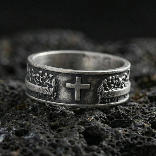 Oxidized sterling silver cross band ring on volcanic stone, macro close-up highlighting darkened recesses, raised cross centerpiece, and crisp relief texture.