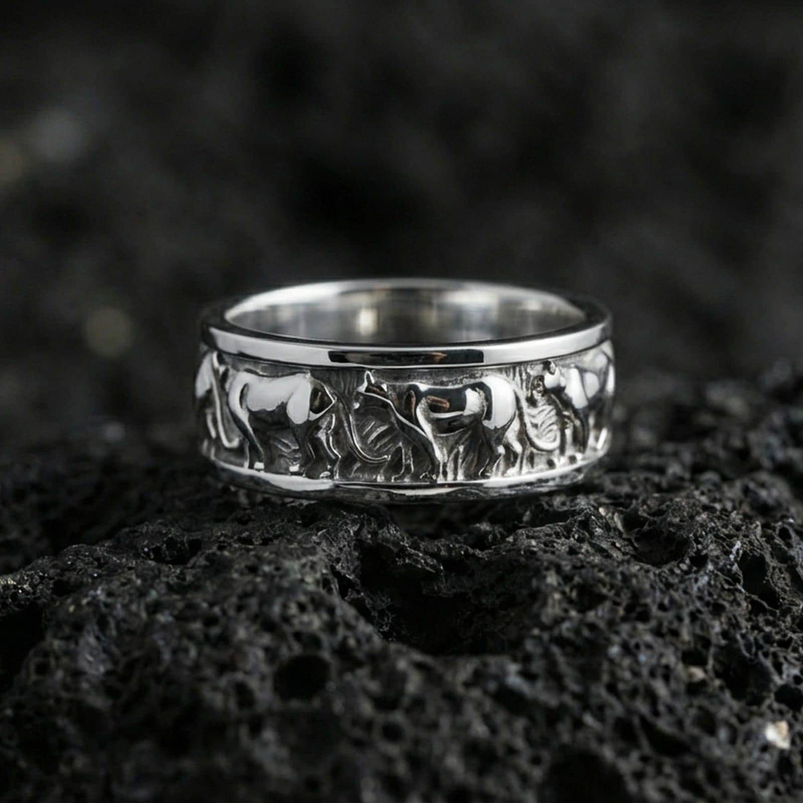 Polished silver horse band ring on volcanic stone, crisp macro shot emphasizing bright reflective edges and the detailed horse silhouettes in clean relief.