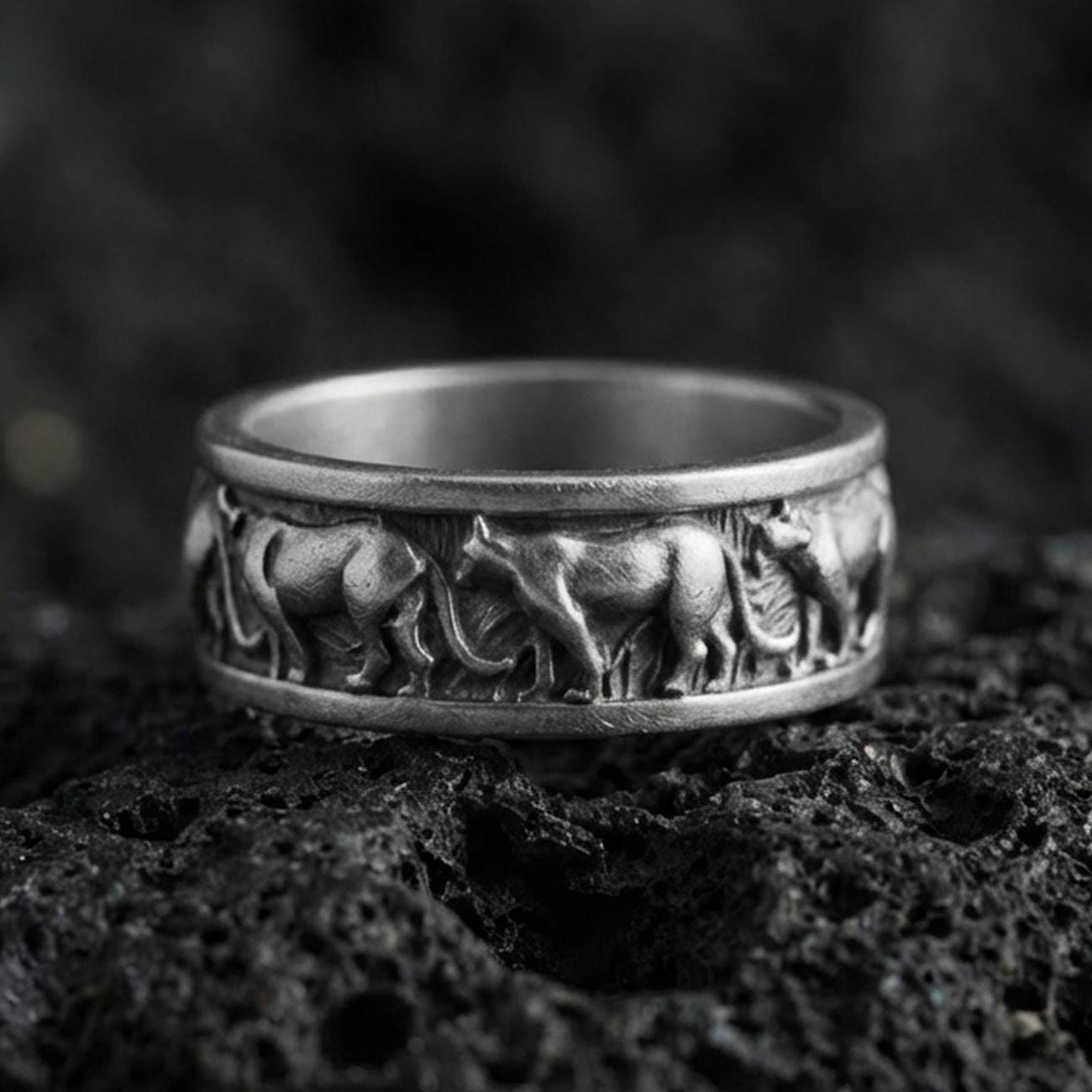Oxidized sterling silver horse band ring on volcanic stone, macro close-up highlighting the darkened recesses and raised running-horse relief around the band.