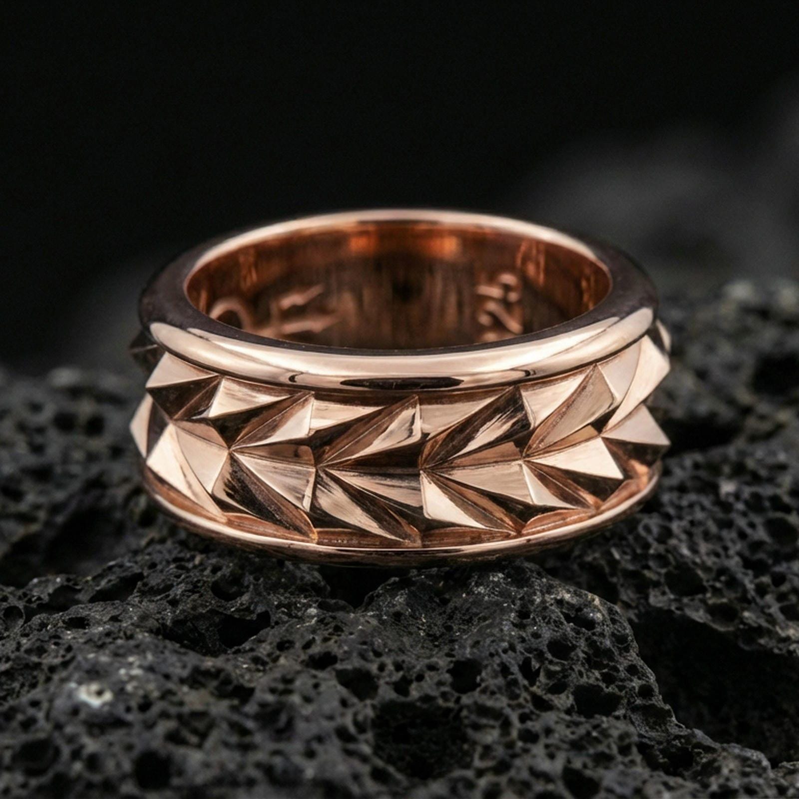 Mechanic style spinning fidget band ring on black volcanic stone, shown in a rose gold plated finish with a softer warm tone that enhances the sculpted faceted pattern.