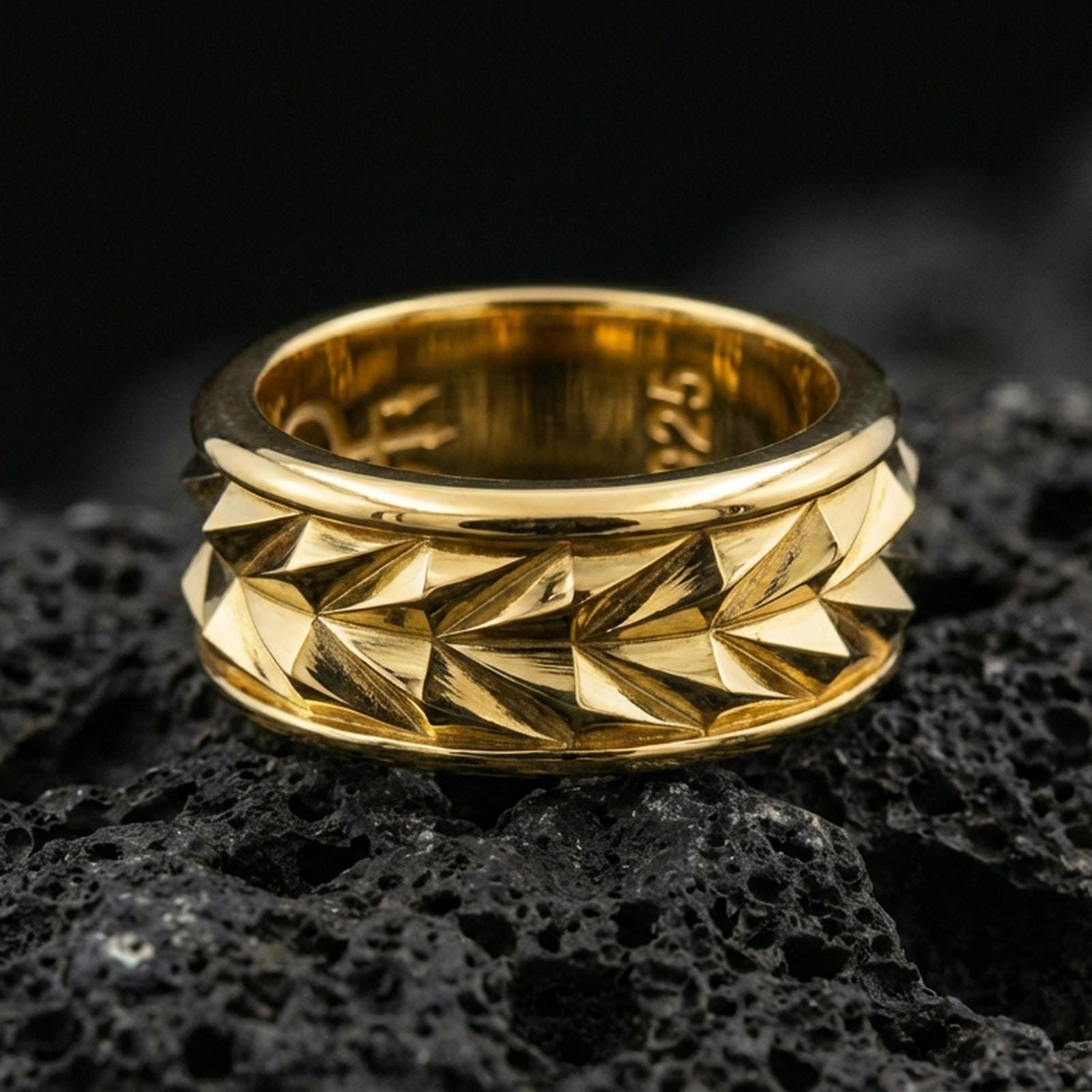 Mechanic style spinning fidget band ring on black volcanic stone, shown in a gold plated finish with warm shine highlighting each angular ridge on the rotating band.