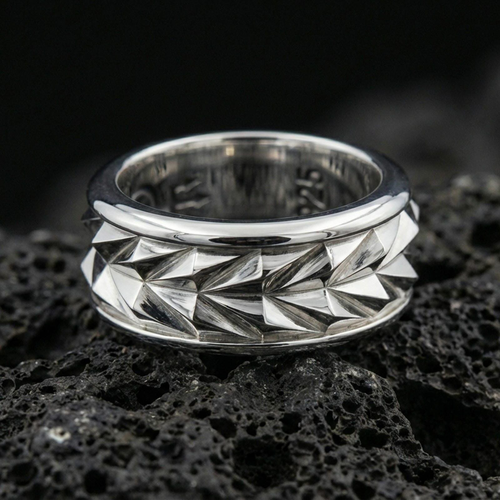 Mechanic style spinning fidget band ring on black volcanic stone, photographed in polished silver with clean reflections across the geometric facets and smooth rounded edges.