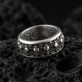 Load image into Gallery viewer, Skull motif sterling silver band ring on black volcanic stone, photographed with an oxidized finish that deepens the skull relief and gothic details.
