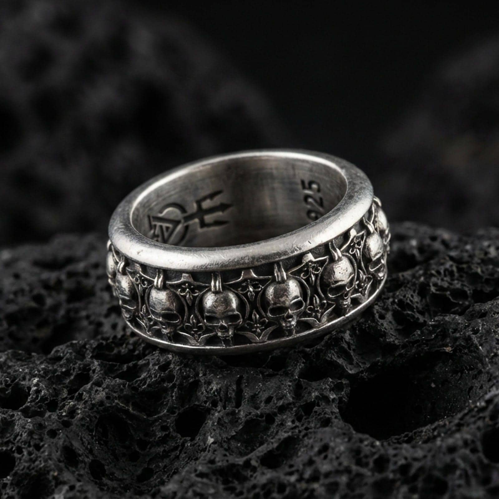 Skull motif sterling silver band ring on black volcanic stone, photographed with an oxidized finish that deepens the skull relief and gothic details.
