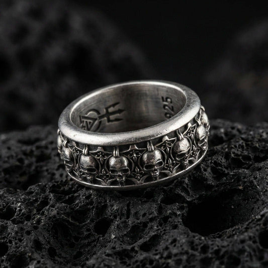 Skull motif sterling silver band ring on black volcanic stone, photographed with an oxidized finish that deepens the skull relief and gothic details.