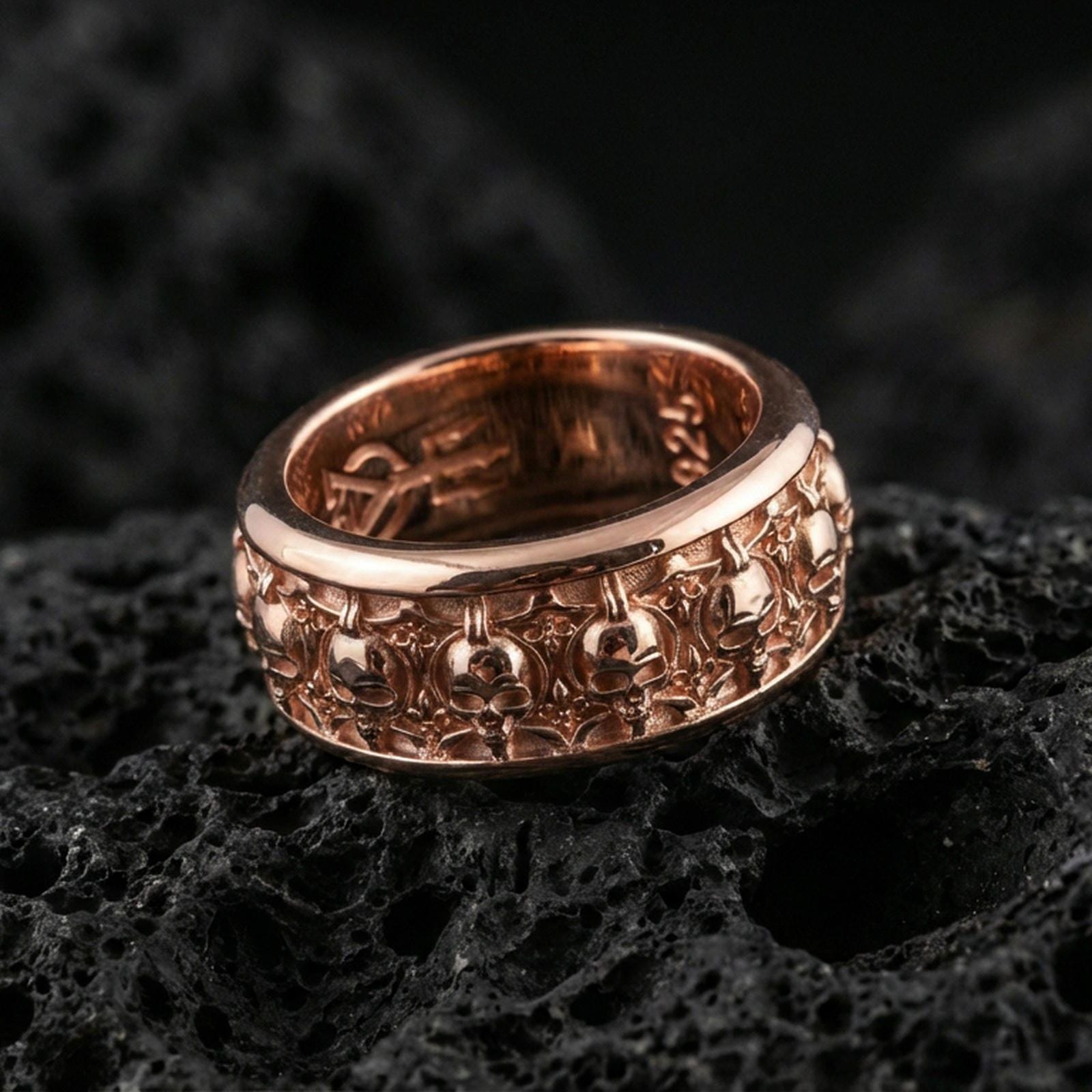 Skull motif sterling silver band ring on black volcanic stone, shown in a rose gold plated finish with a softer warm tone outlining each skull detail.
