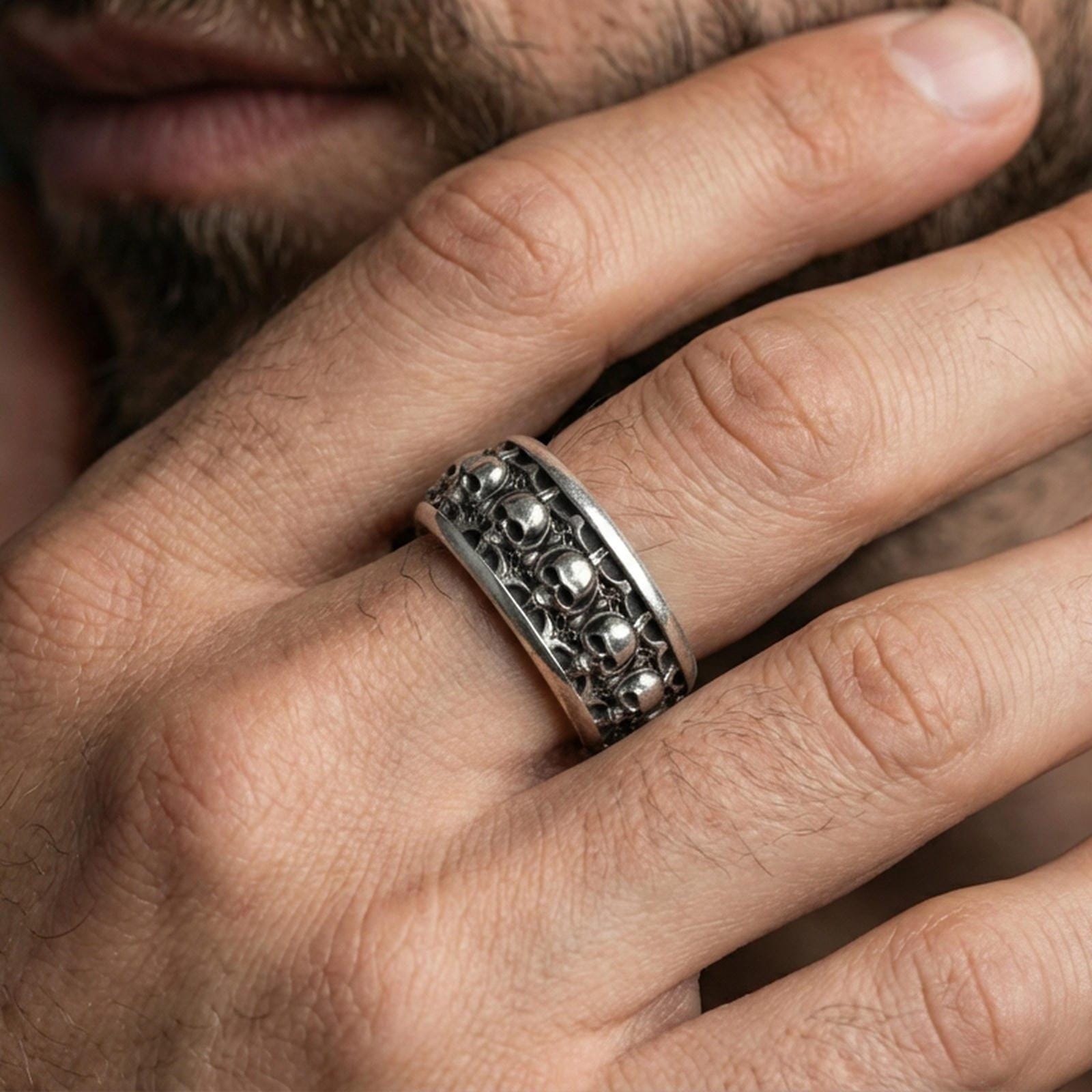 Skull motif sterling silver band ring worn on a finger, oxidized sterling silver look with high-contrast shadows emphasizing the gothic skull row.