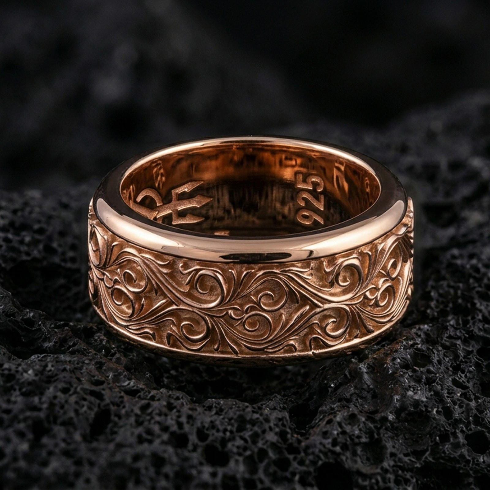 Ornate scrollwork sterling silver band ring on black volcanic stone, shown in a rose gold plated finish with a softer warm tone accenting the ornamental curves.