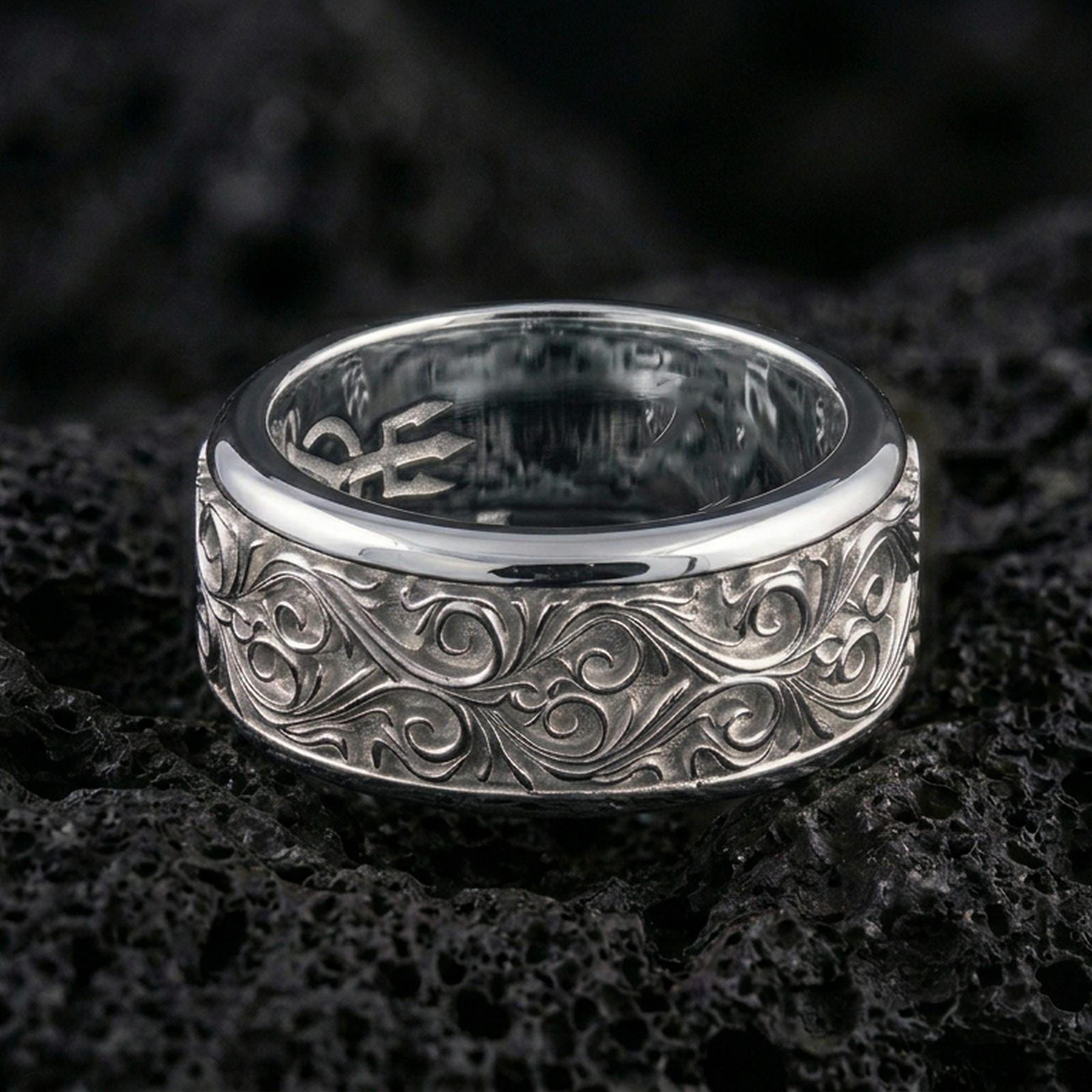 Ornate scrollwork sterling silver band ring on black volcanic stone, photographed in a polished silver look with clean highlights across the flowing vine-like details.