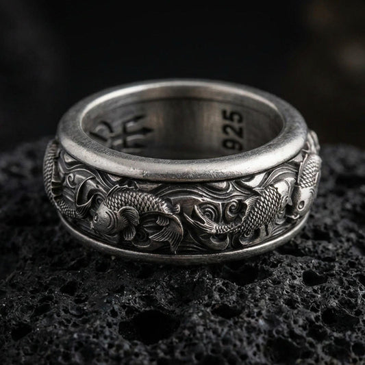 Koi fish sterling silver band ring on black volcanic stone, photographed with an oxidized finish to emphasize contrast in the carved scales and flowing water waves.