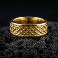 Load image into Gallery viewer, Sterling silver Celtic knot band ring on black volcanic stone, presented in a gold plated finish with warm shine that enhances the Celtic weave and dimensional relief.
