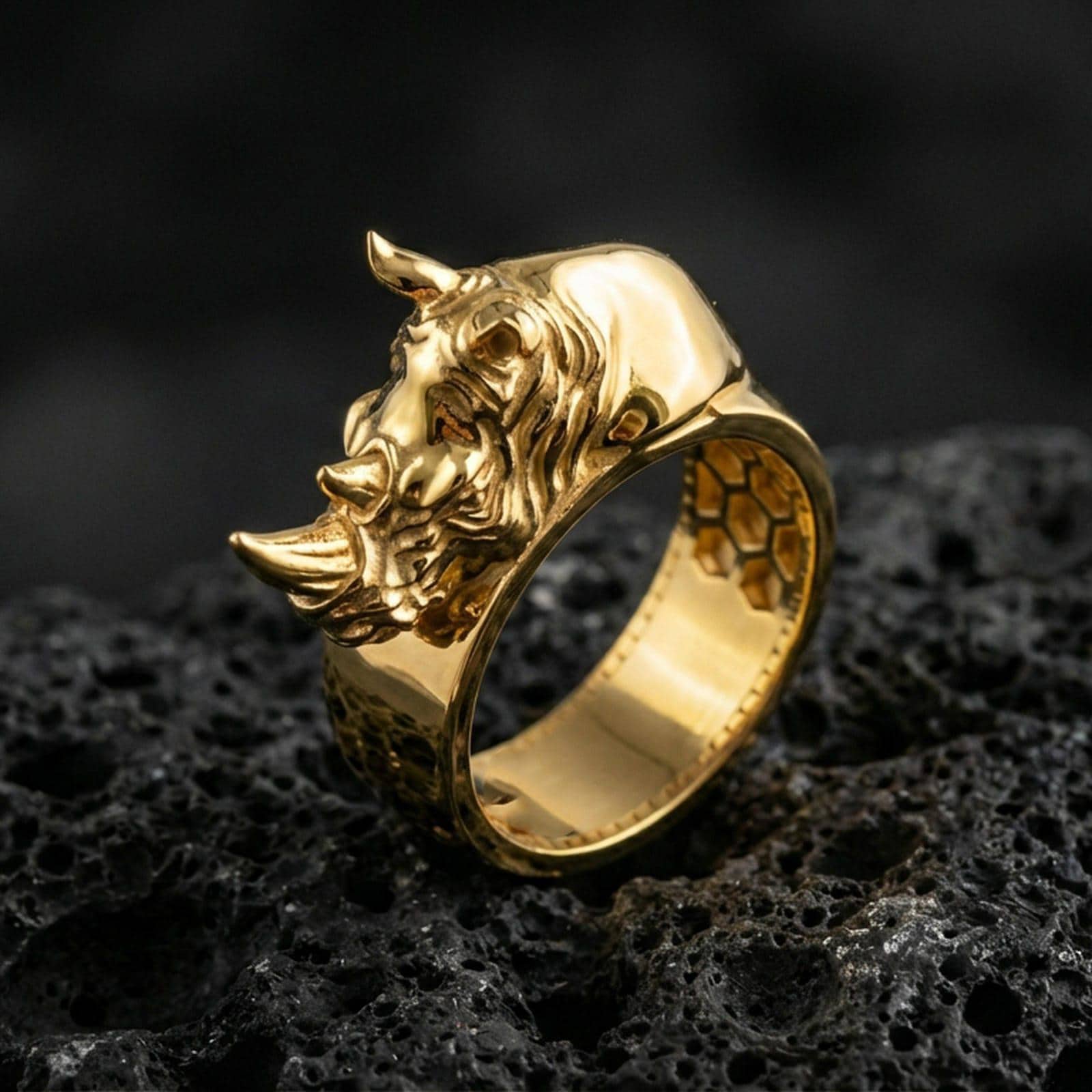 Sterling silver rhino head ring photographed on black volcanic stone, shown in a gold plated finish that emphasizes the rhino head relief and premium shine.