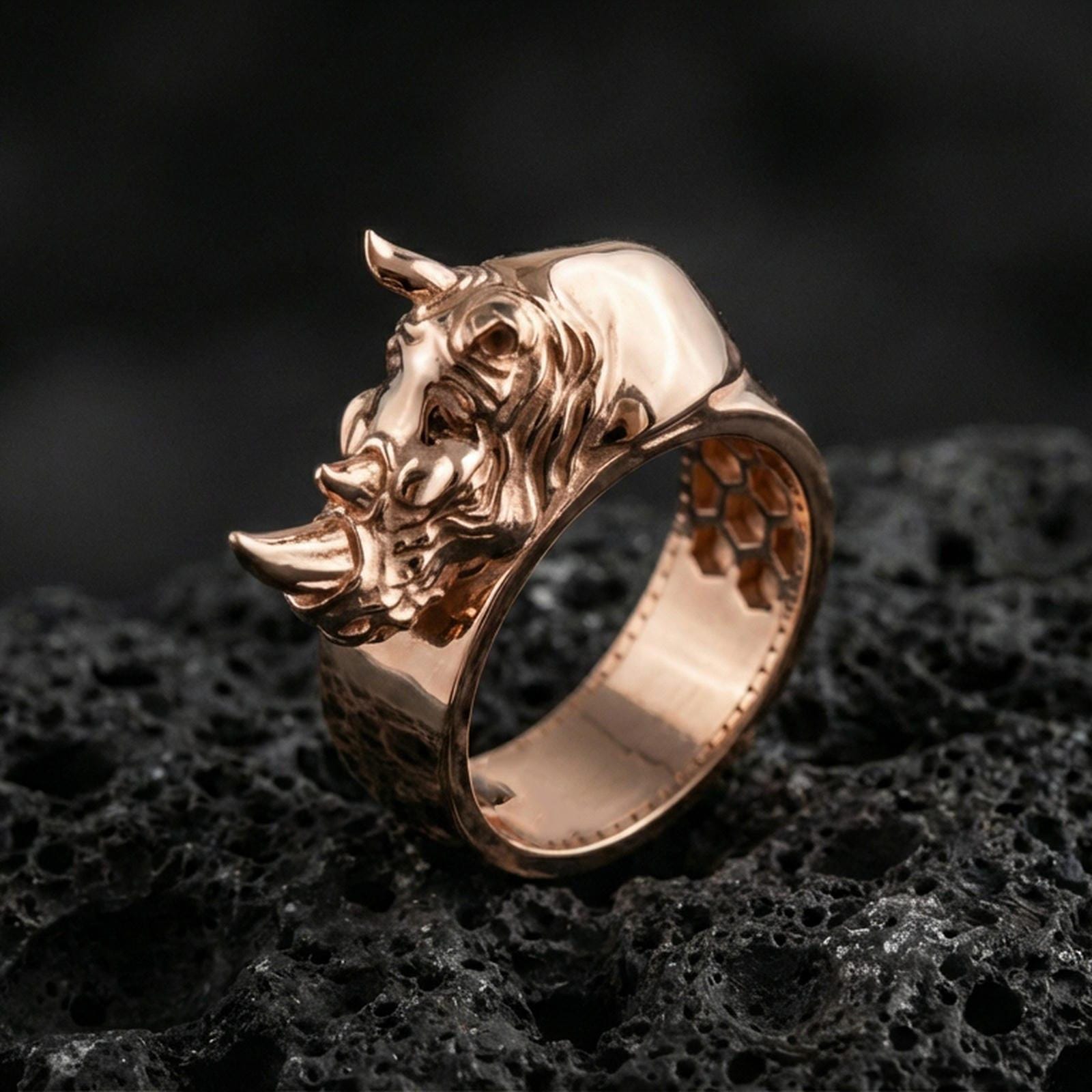 Sterling silver rhino head ring photographed on black volcanic stone, shown in a rose gold plated finish with warm reflections that enhance the sculpted rhino details.