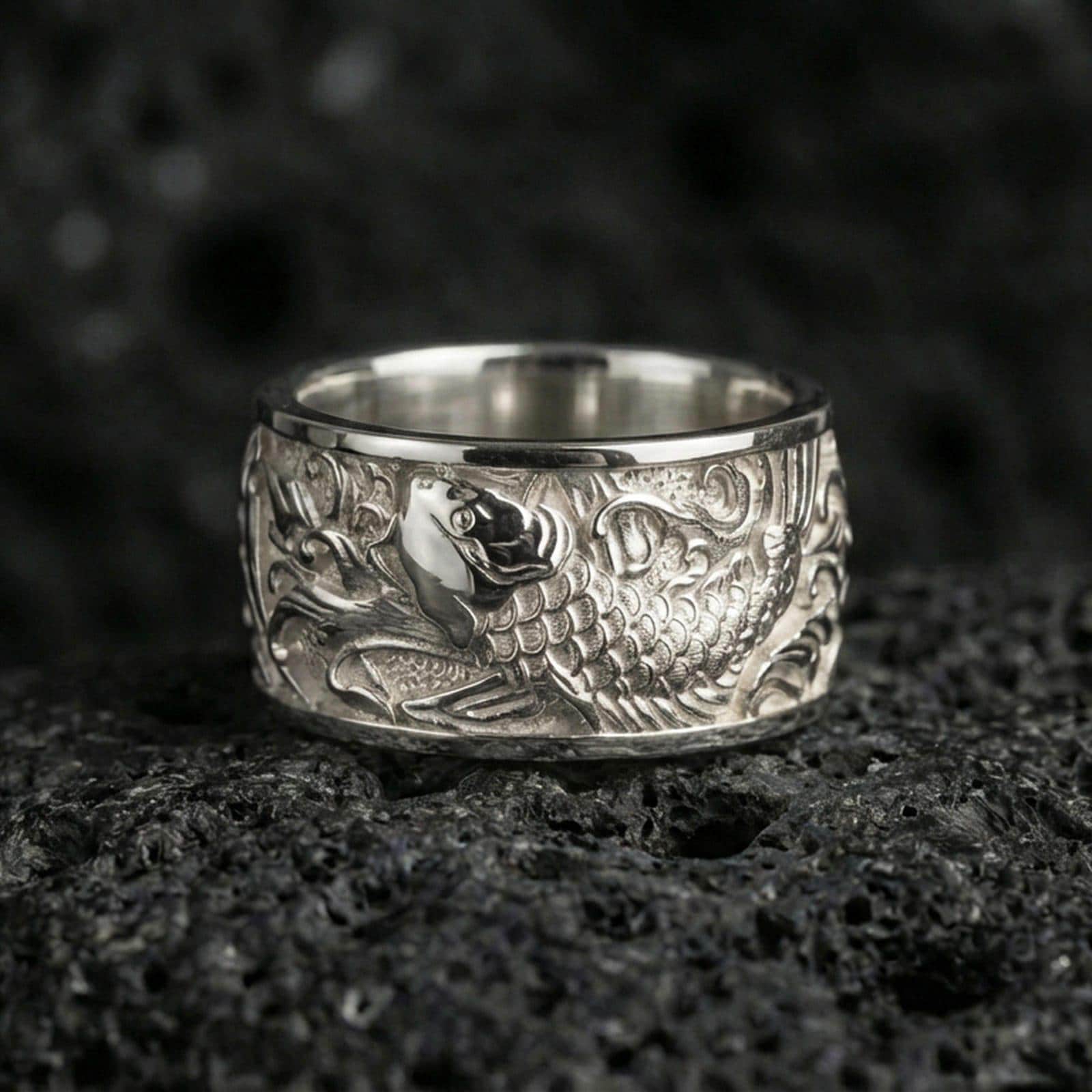 Koi fish spinner band ring on black volcanic stone, shown in a polished silver finish with clean highlights across the raised koi relief.