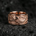 Load image into Gallery viewer, Koi fish spinner band ring on black volcanic stone, shown in a rose gold plated finish with soft warm reflections on the engraved koi pattern.
