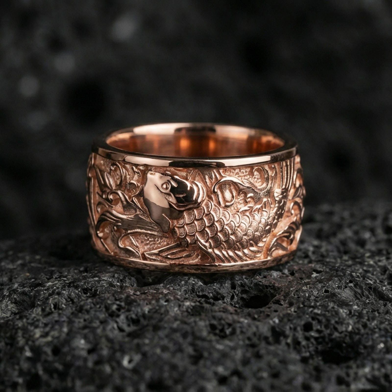 Koi fish spinner band ring on black volcanic stone, shown in a rose gold plated finish with soft warm reflections on the engraved koi pattern.