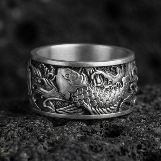 Koi fish spinner band ring on black volcanic stone, shown in an oxidized sterling silver finish with deep contrast around the carved scales.