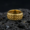 Load image into Gallery viewer, Celtic knot spinner band ring on black volcanic stone, shown in a gold plated finish with warm shine emphasizing the braided Celtic pattern.
