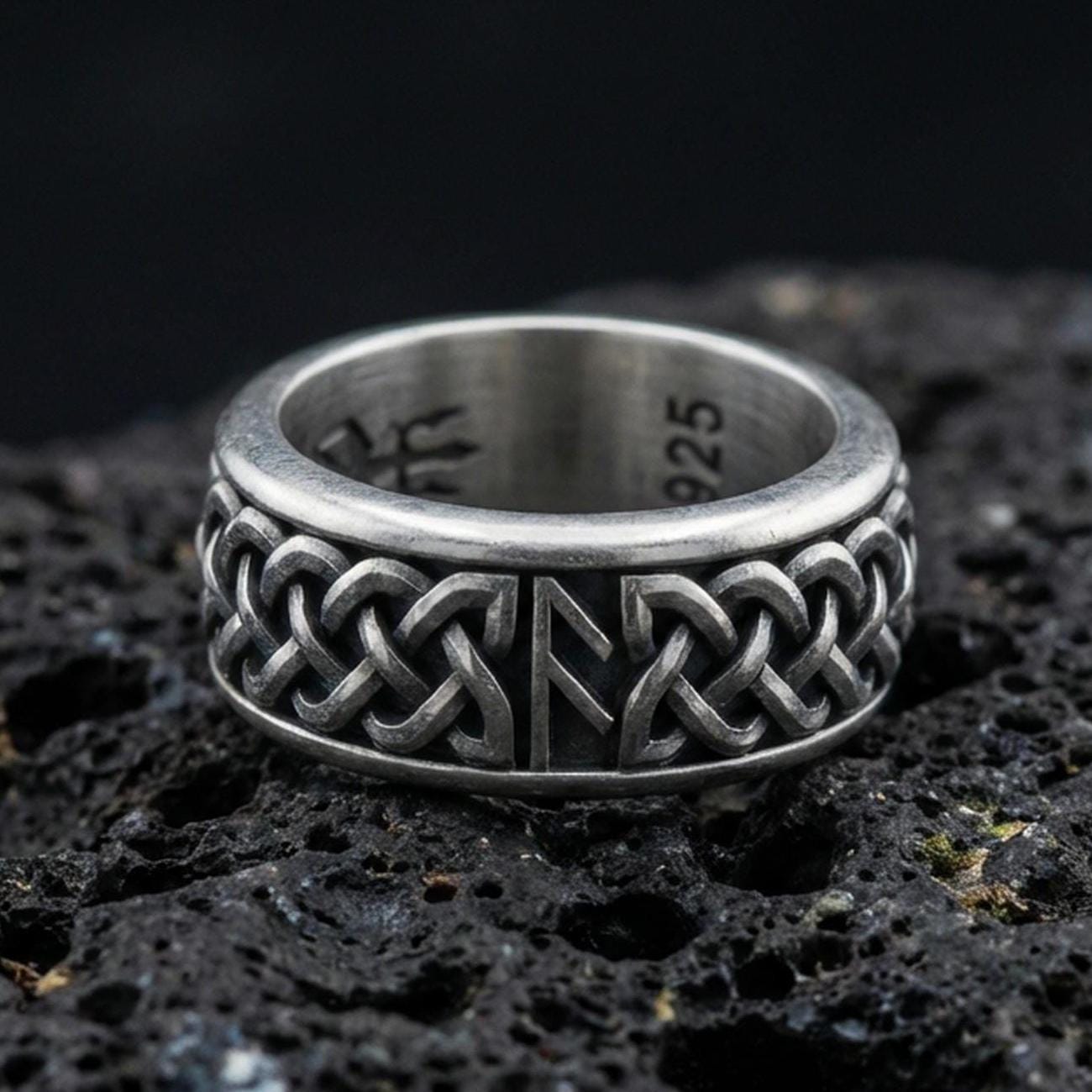 Celtic knot spinner band ring on black volcanic stone, shown in an oxidized sterling silver finish with deep darkened recesses highlighting the interlaced braid.