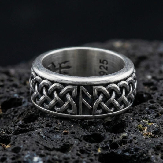 Celtic knot spinner band ring on black volcanic stone, shown in an oxidized sterling silver finish with deep darkened recesses highlighting the interlaced braid.
