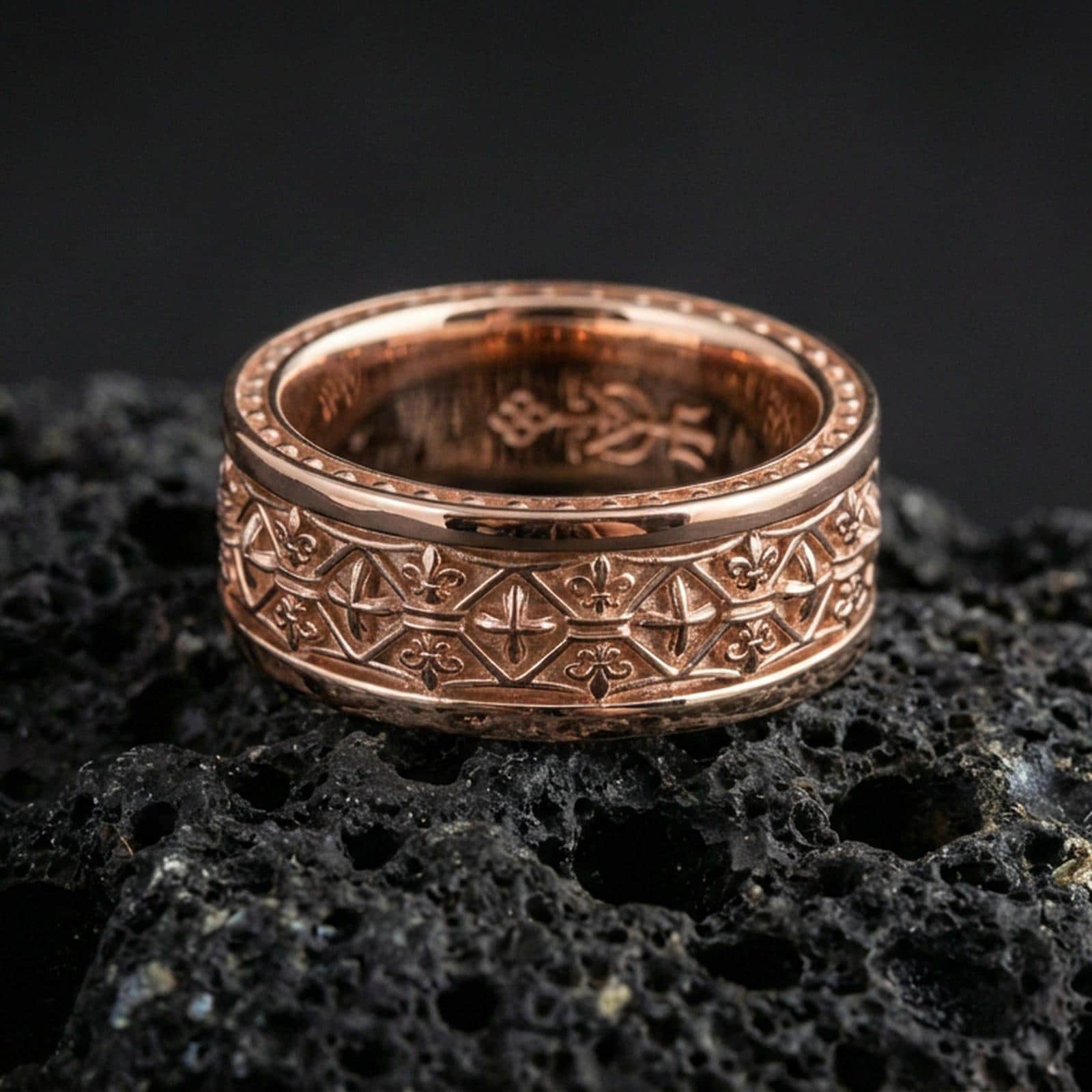 Gothic fleur-de-lis band ring on black volcanic stone, shown in a rose gold plated finish with a soft warm tone that enhances the engraved medieval geometry.