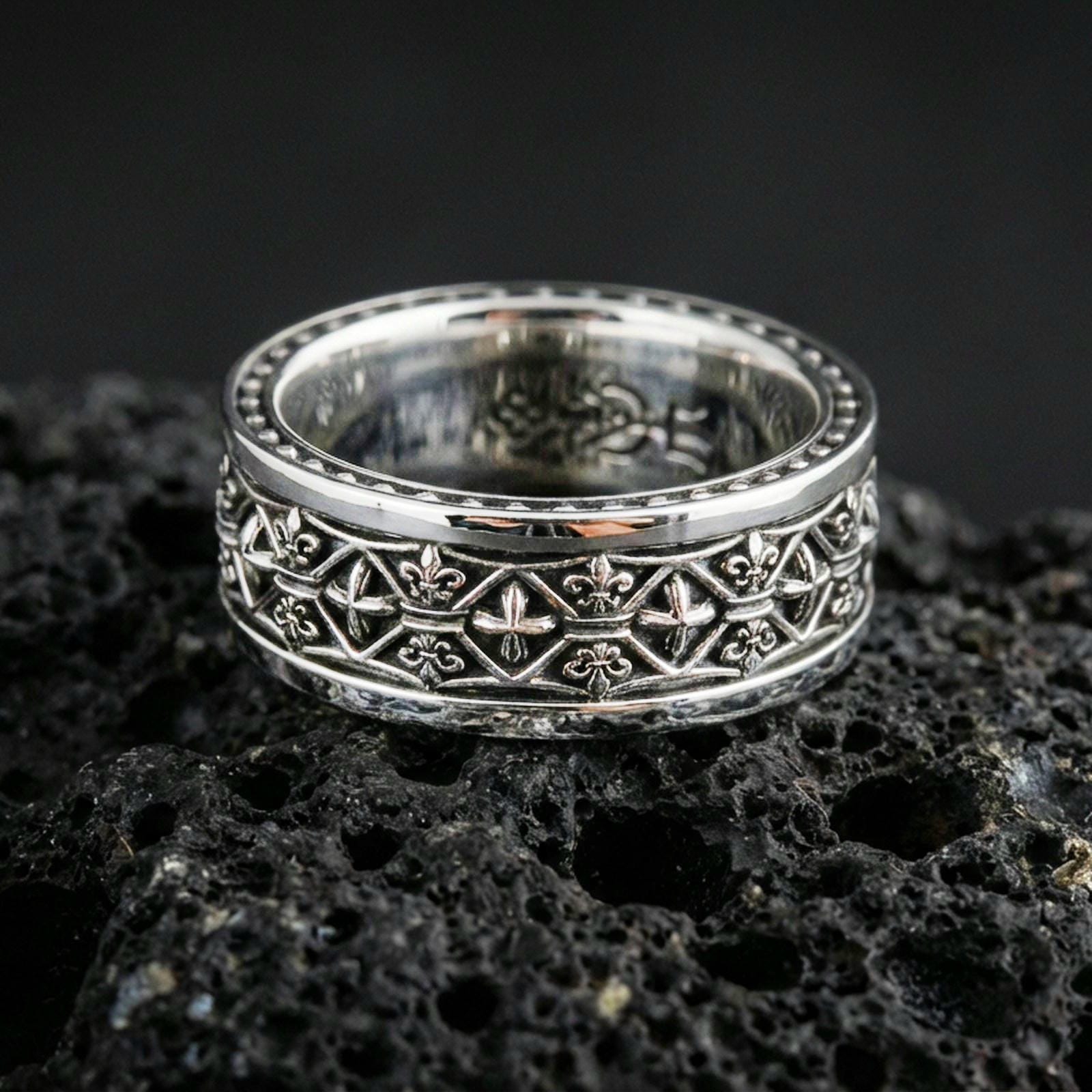 Gothic fleur-de-lis band ring on black volcanic stone, shown in a polished silver finish with crisp reflective edges across the raised fleur-de-lis pattern.