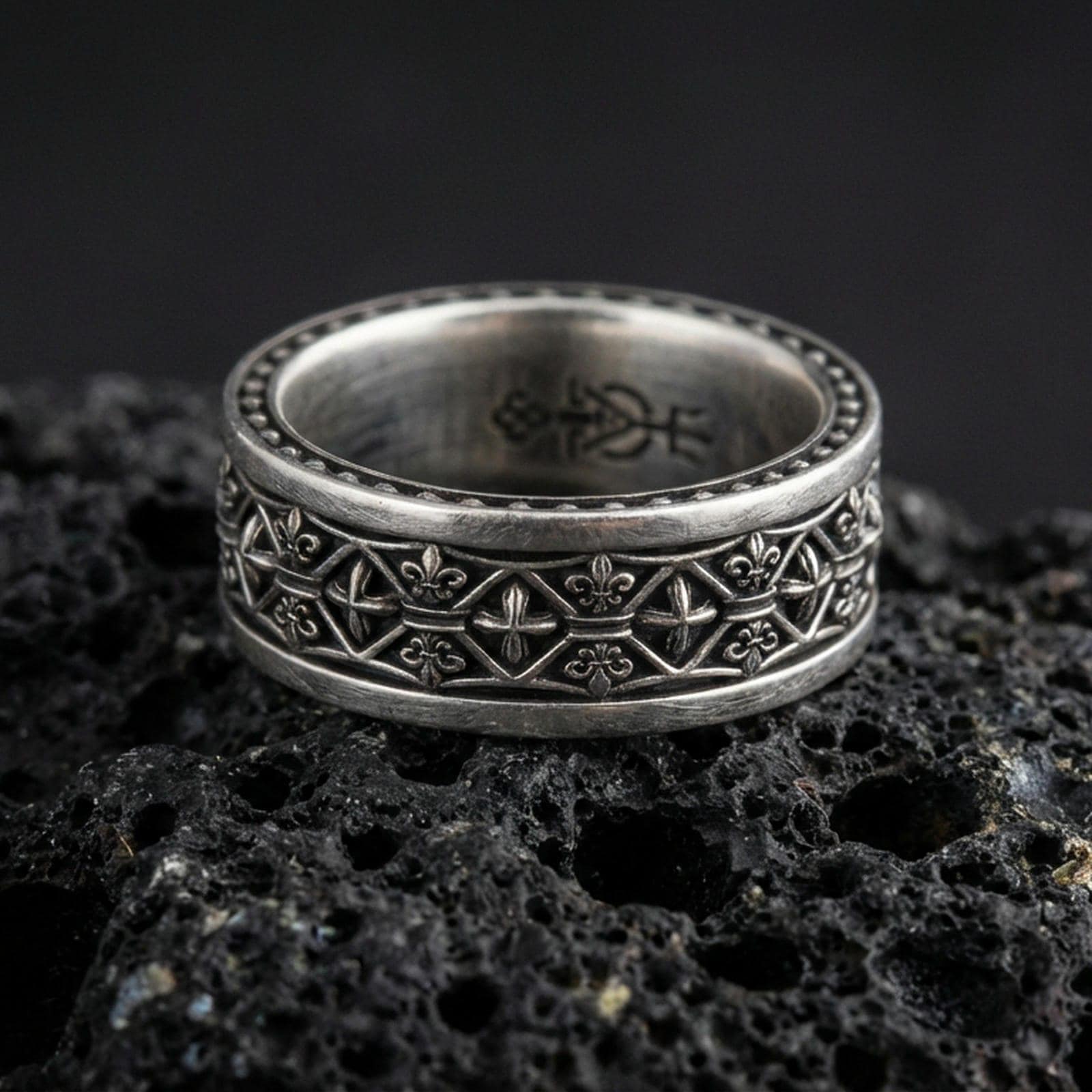 Gothic fleur-de-lis band ring on black volcanic stone, shown in an oxidized sterling silver finish with deep darkened recesses emphasizing the medieval lattice details.