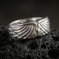 Load image into Gallery viewer, Angel wing sterling silver band ring on black volcanic stone, shown in a polished silver finish with crisp highlights across each feather ridge.
