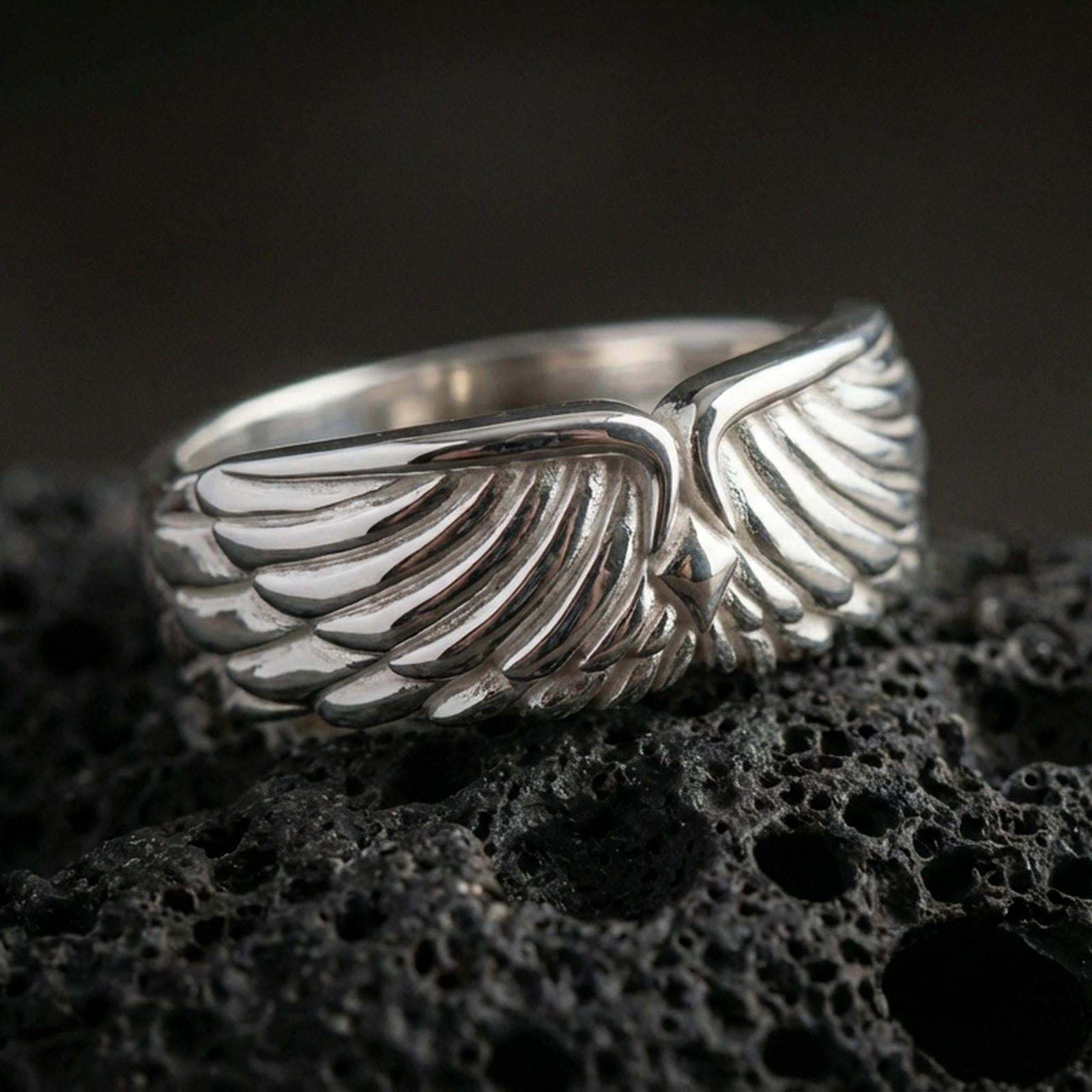 Angel wing sterling silver band ring on black volcanic stone, shown in a polished silver finish with crisp highlights across each feather ridge.