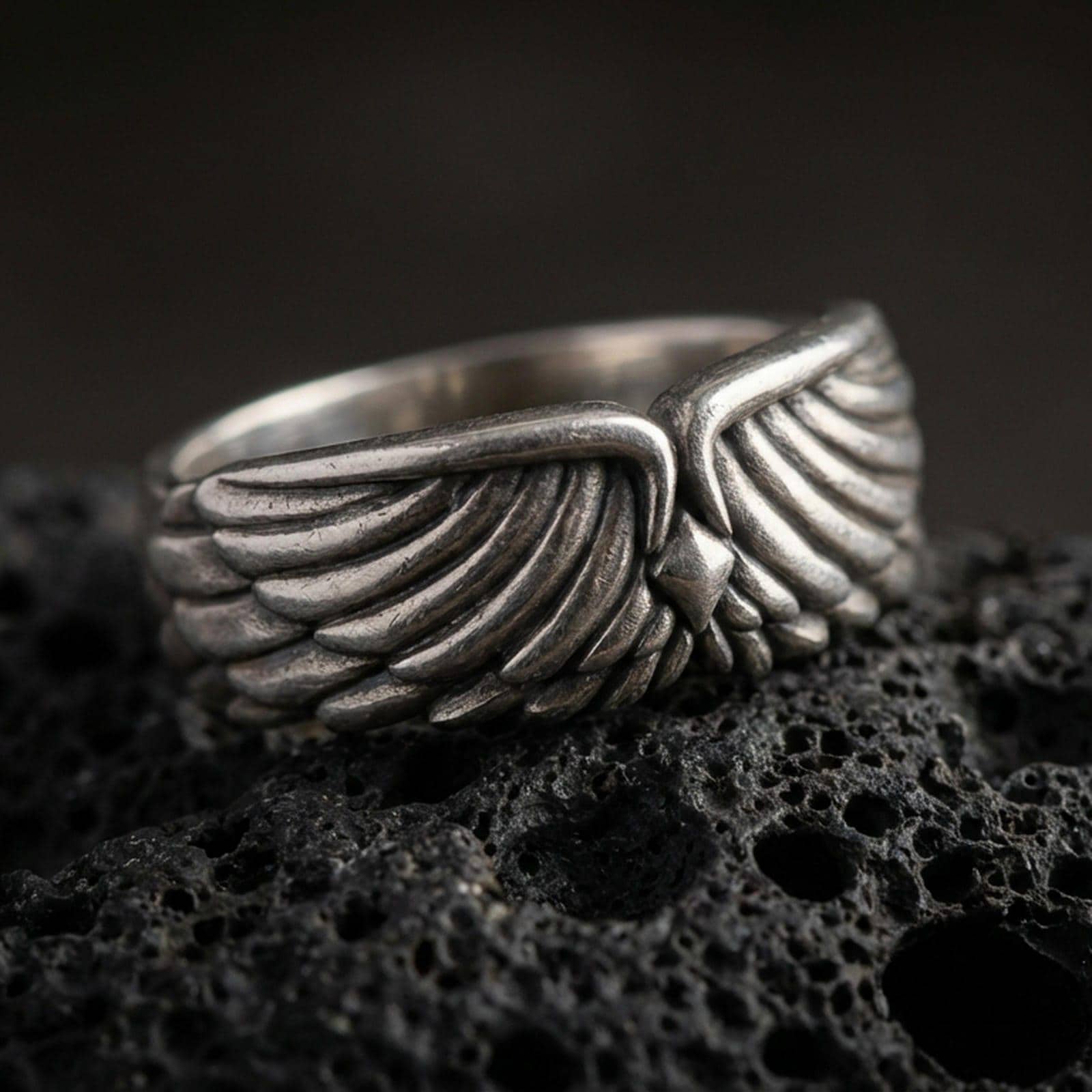 Angel wing sterling silver band ring on black volcanic stone, shown in an oxidized finish with deepened shadows between the feather layers for strong contrast.