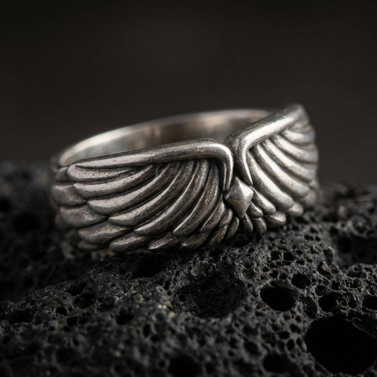 Angel wing sterling silver band ring on black volcanic stone, shown in an oxidized finish with deepened shadows between the feather layers for strong contrast.