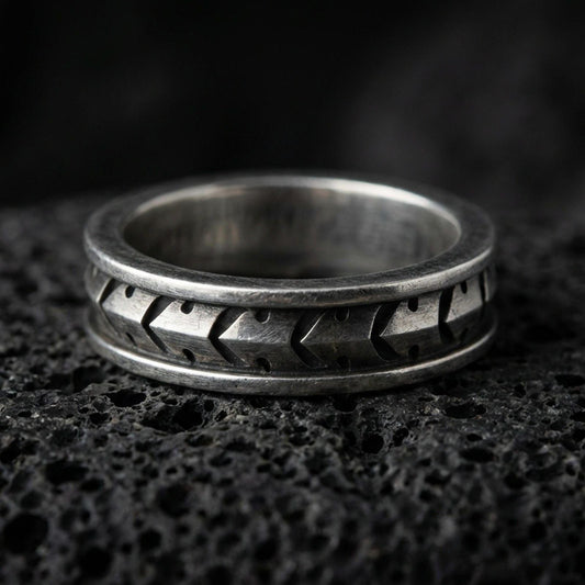 Industrial tread pattern sterling silver spinner ring on black volcanic stone, shown with an oxidized finish that emphasizes the recessed grooves and mechanical depth.