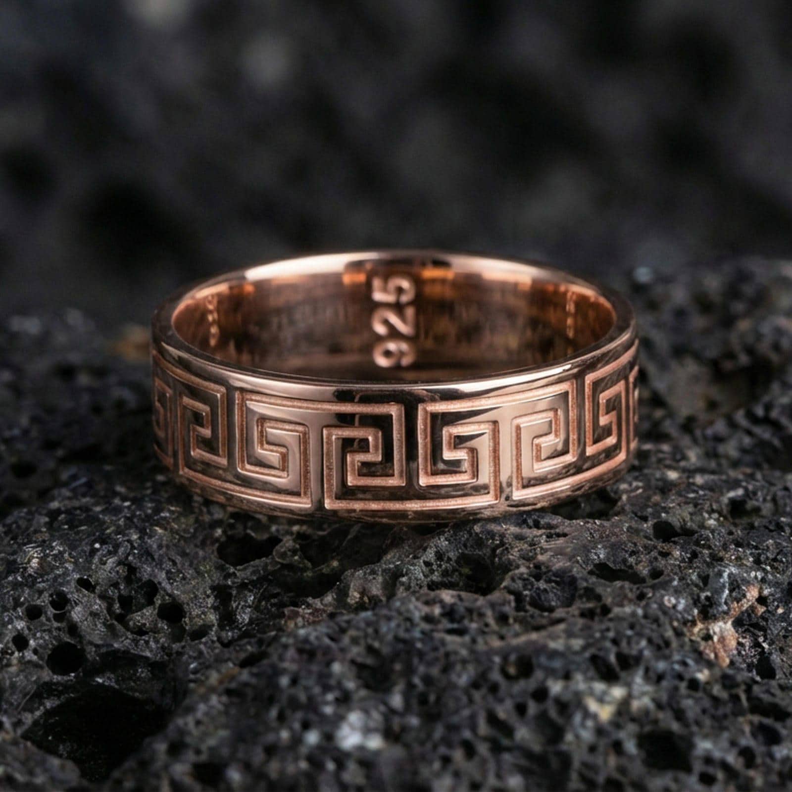 Rose gold plated sterling silver Greek key band on volcanic stone, sharp geometric meander engraving, minimal high-end close-up.