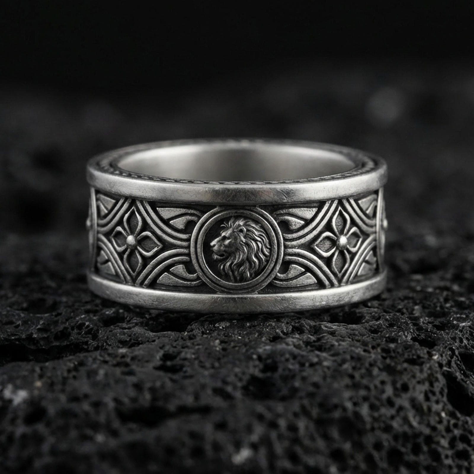 Oxidized sterling silver lion medallion band ring on dark volcanic rock, ornate Gothic arch and quatrefoil engraving, premium macro product shot.