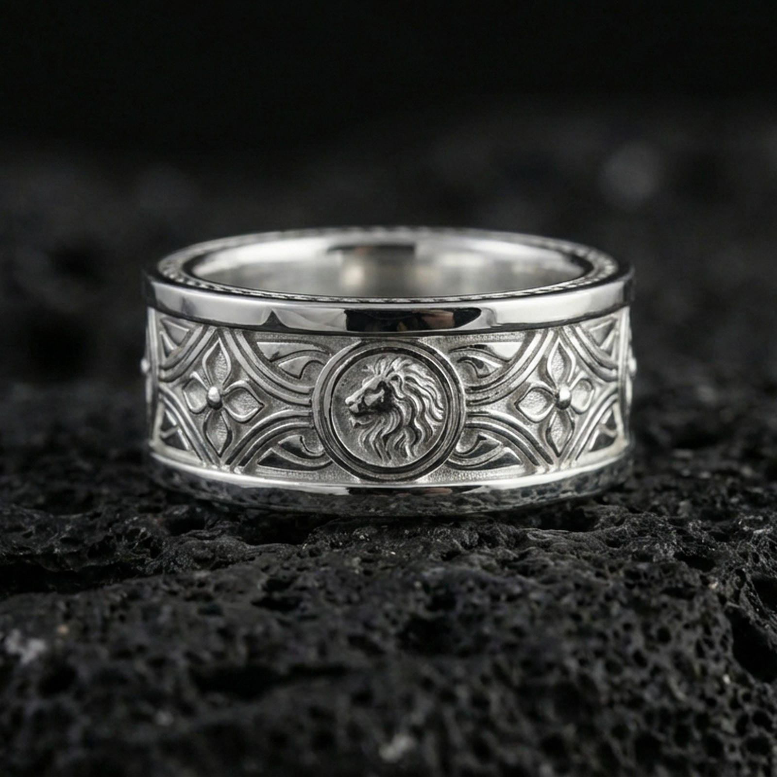 Polished silver lion head medallion band on black volcanic stone, crisp ornamental scrollwork and geometric accents, centered close-up studio lighting.