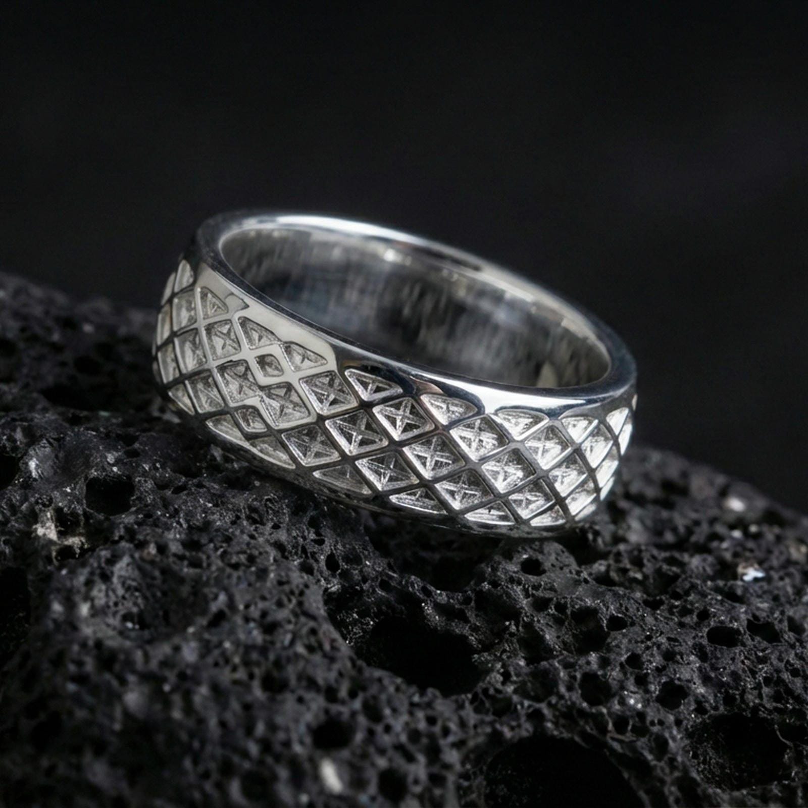Polished silver lattice pattern band ring on black volcanic stone, crisp diamond grid texture and clean borders, centered close-up studio lighting.