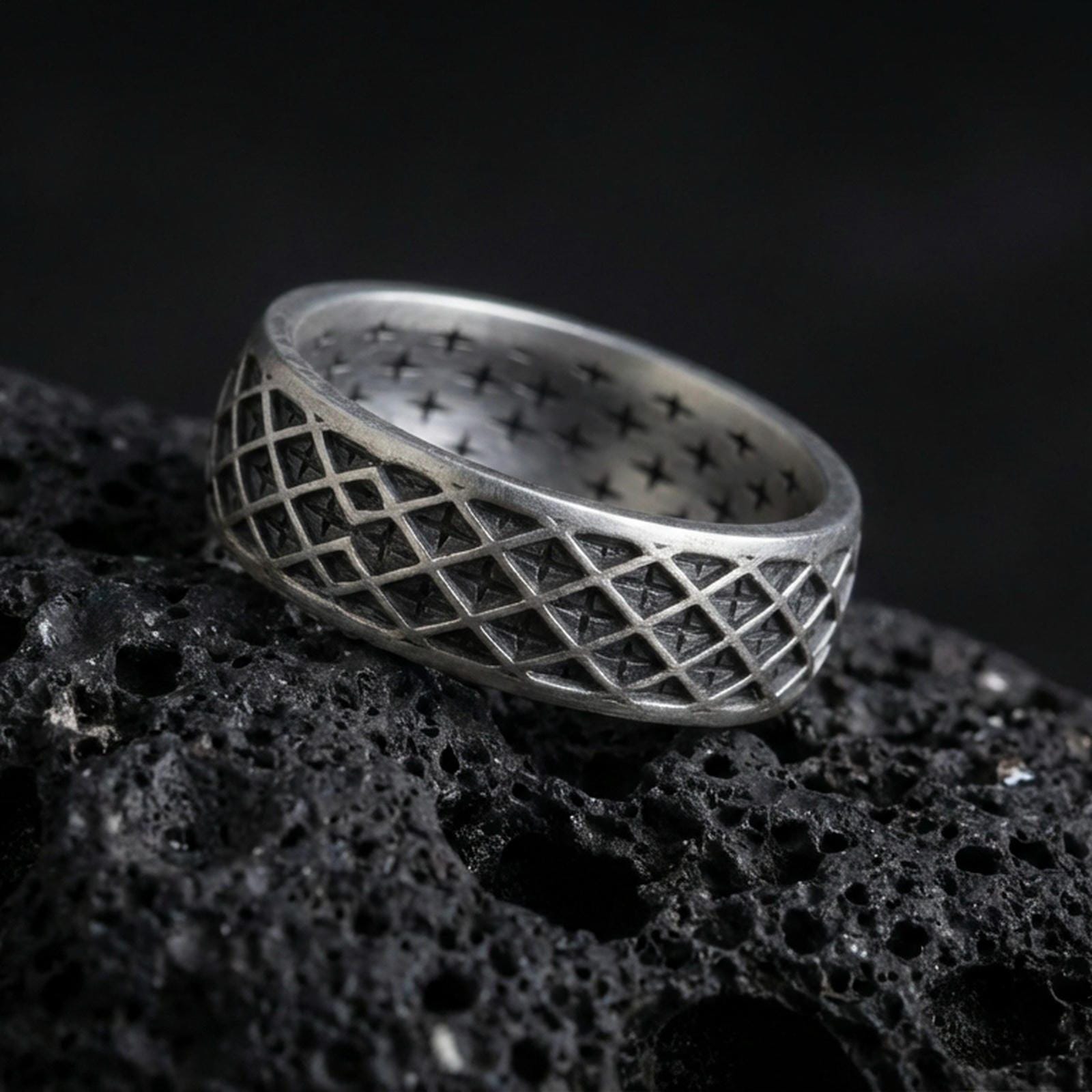 Oxidized sterling silver geometric lattice band ring on dark volcanic rock, diamond grid engraving with deep contrast, premium macro product shot.