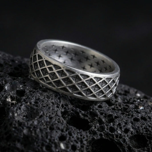 Oxidized sterling silver geometric lattice band ring on dark volcanic rock, diamond grid engraving with deep contrast, premium macro product shot.