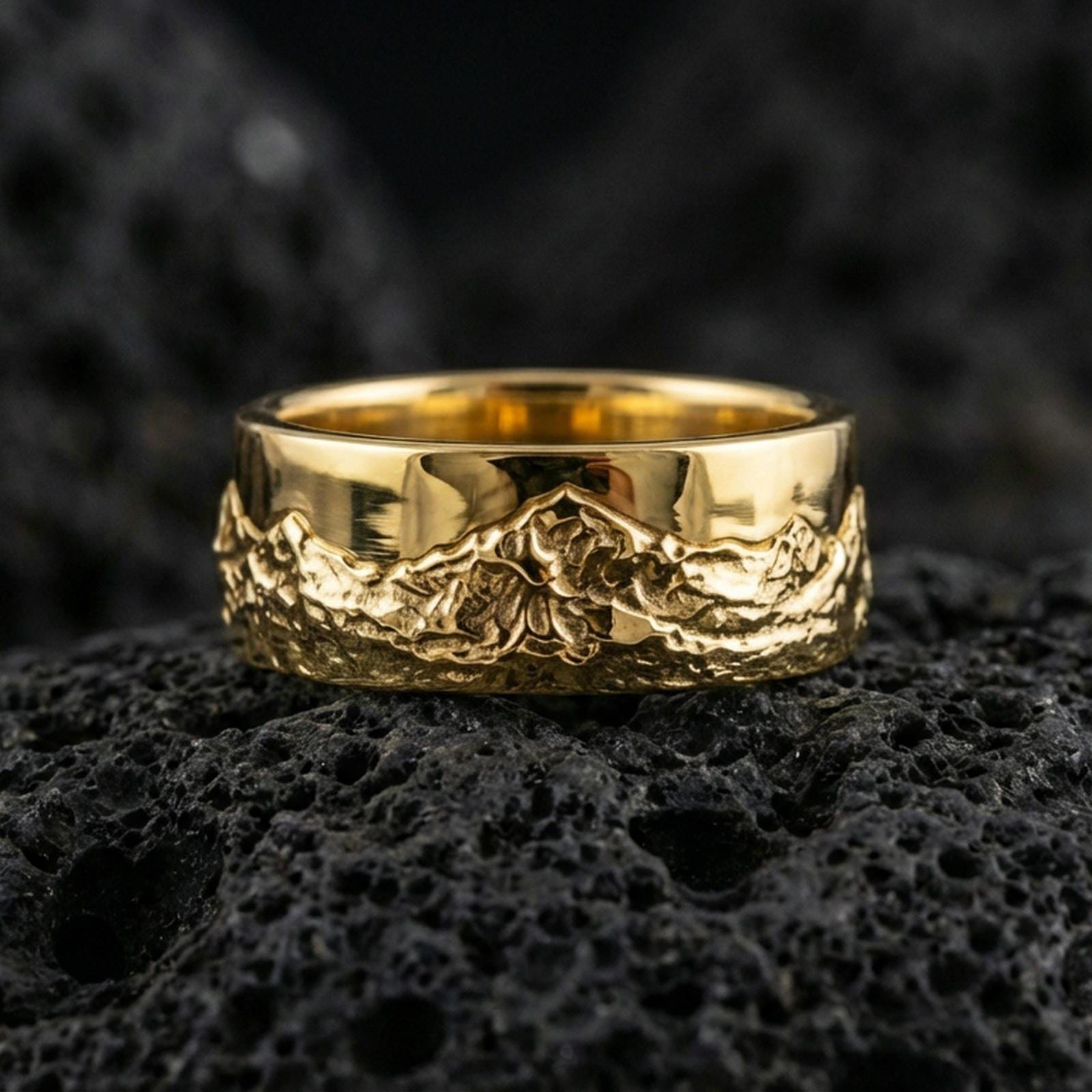 Gold plated mountain landscape band ring on volcanic rock, detailed peak relief and textured valley scene, luxury jewelry product photography.