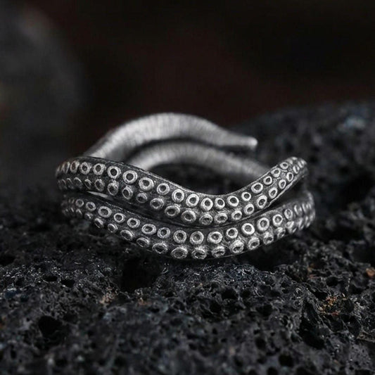 Oxidized sterling silver octopus tentacle wrap ring on dark volcanic rock, suction cup texture detail, premium macro product shot.