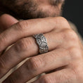 Load image into Gallery viewer, Oxidized sterling silver engraved ornament band worn on finger, raised diamond panel detail, natural lifestyle hand shot with shallow depth of field.
