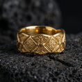 Load image into Gallery viewer, Gold plated ornate engraved band ring on volcanic rock, raised diamond pattern with decorative scroll accents, luxury jewelry product photography.
