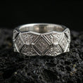 Load image into Gallery viewer, Polished silver geometric engraved band ring on black volcanic stone, crisp faceted diamond motifs and ornate scroll engraving, centered close-up studio lighting.
