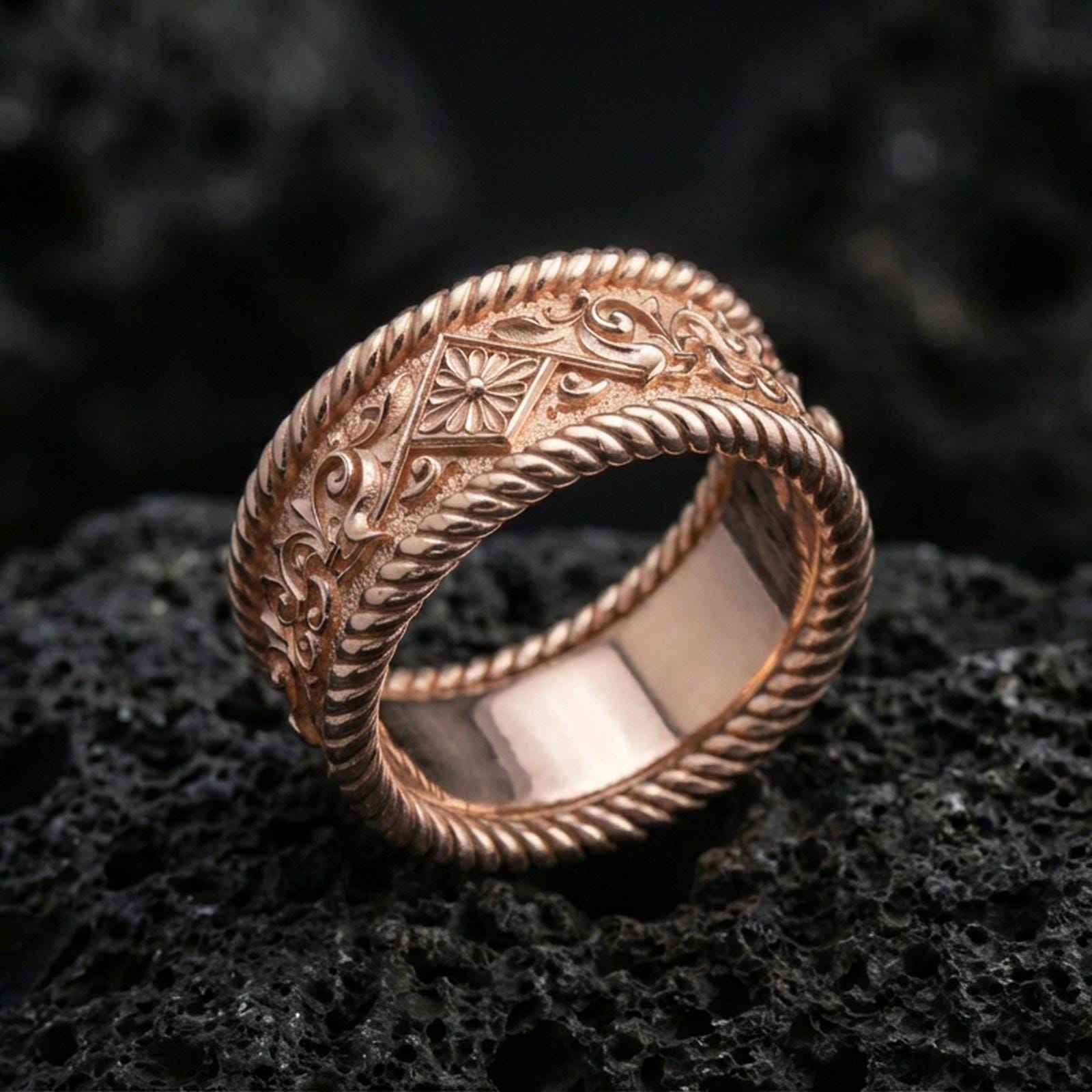 Rose gold plated sterling silver rope border ring on volcanic stone, intricate floral and filigree engraving with deep contrast, minimal high-end close-up.