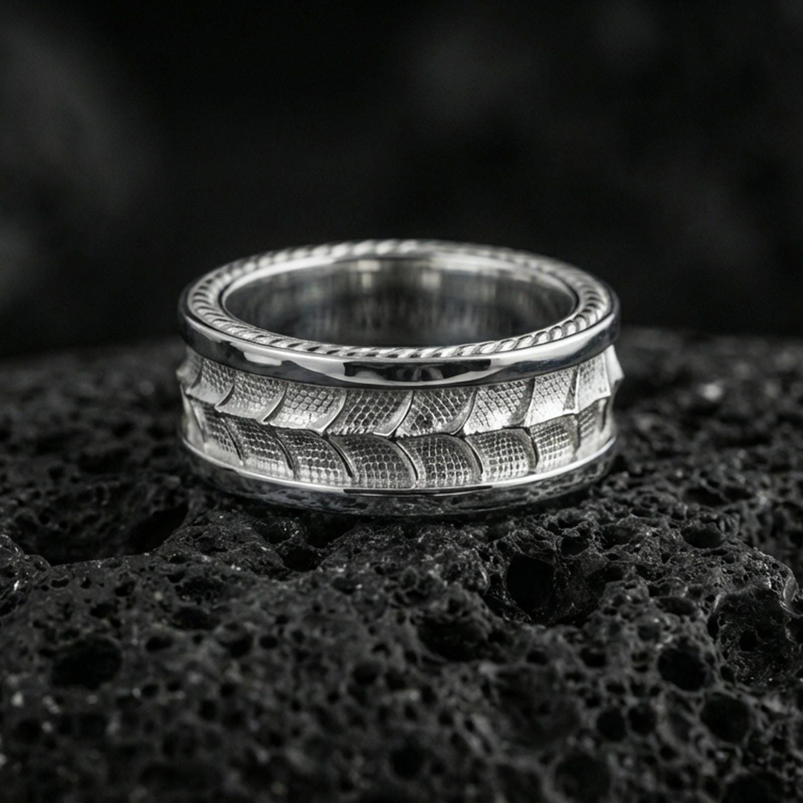 Polished silver snake scale texture band ring on black volcanic stone, crisp reptile pattern engraving and clean borders, centered close-up studio lighting.